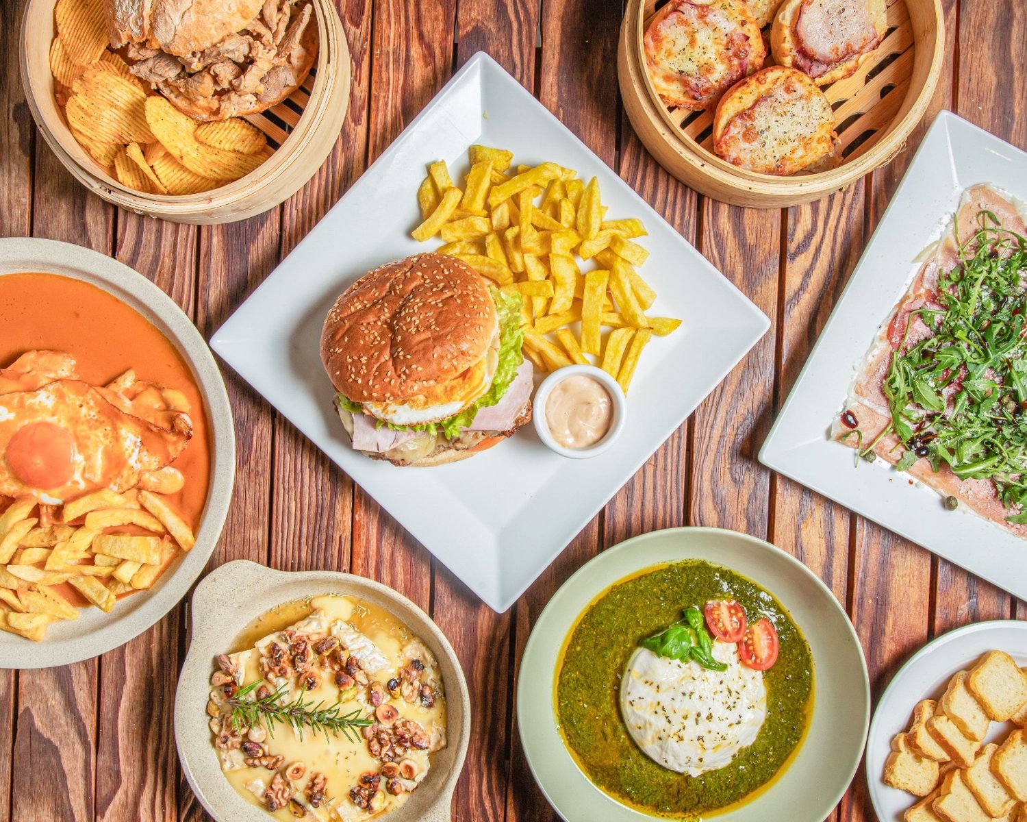 Mesa com pizza, hambúrguer, entradas e sobremesas